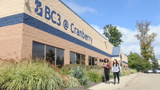 Two students walking together on the sidewalk outside the exterior wall of the Cranberry campus brick building with the name "BC3 @ Cranberry" on the building in blue letters