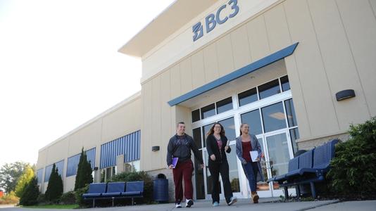 Students at Lawrence Crossing exiting the front doors to the building with the word "BC3" on the building in the background in blue letters on the wall of the white building