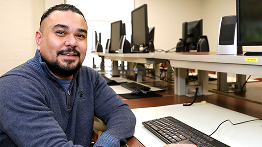 Image: portrait of a male student sitting at a desk with a computer keyboard