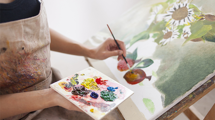 Image: an artist holding a palette painting a picture flowers and fruits