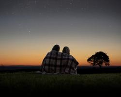 couple sitting under the stars wrapped in a blanket facing away from the camera