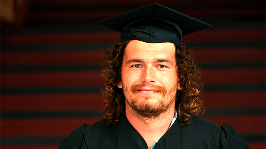 Image: photo of a male graduate wearing a black cap and gown