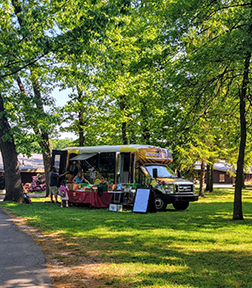 The Produce Cart food truck with produce displayed on tables in the Art and Hospitality loop with oak trees in the background. 